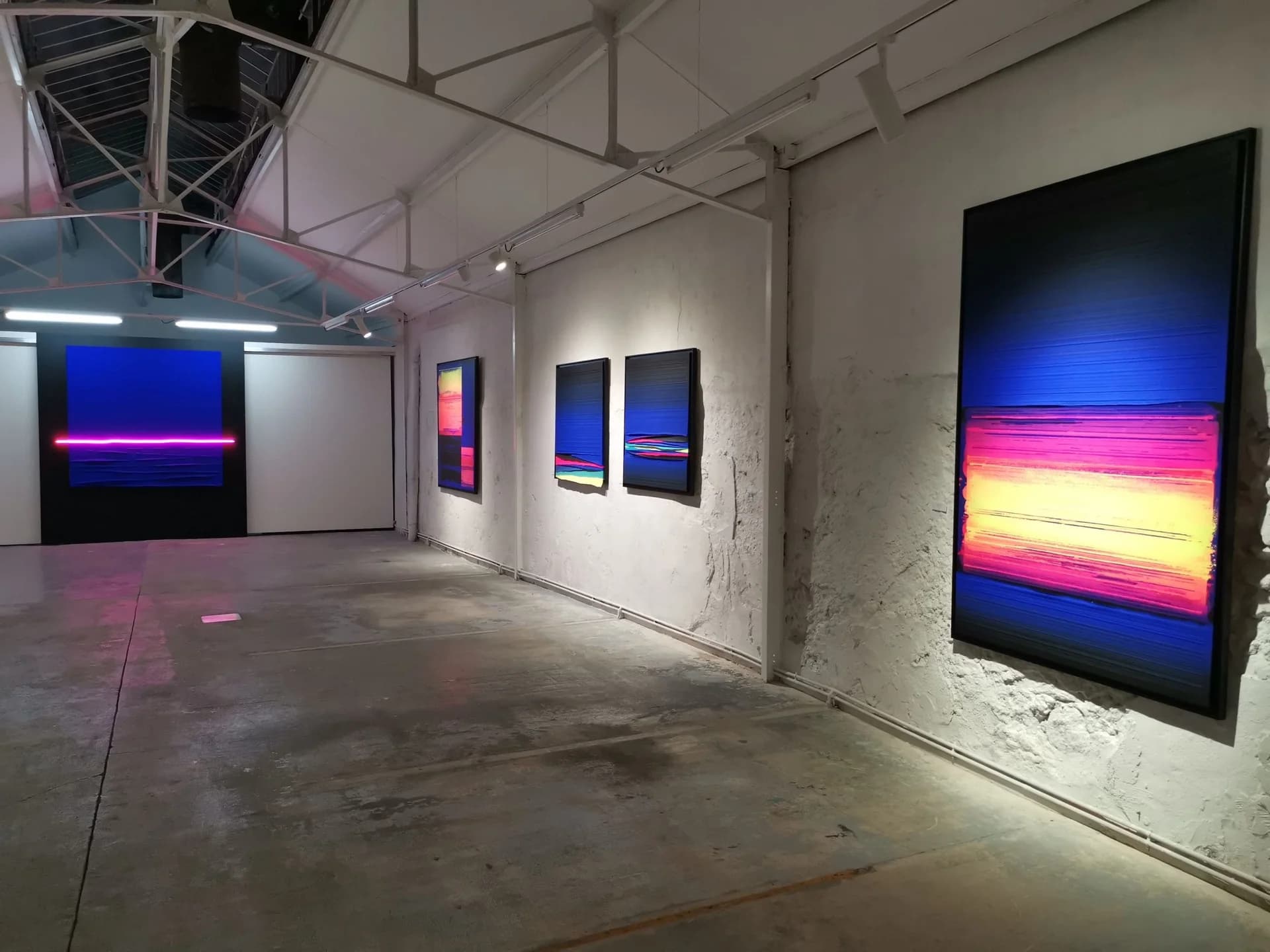 Installation view at Galerie Diego Escobar with luminous horizon-like paintings in a concrete gallery.